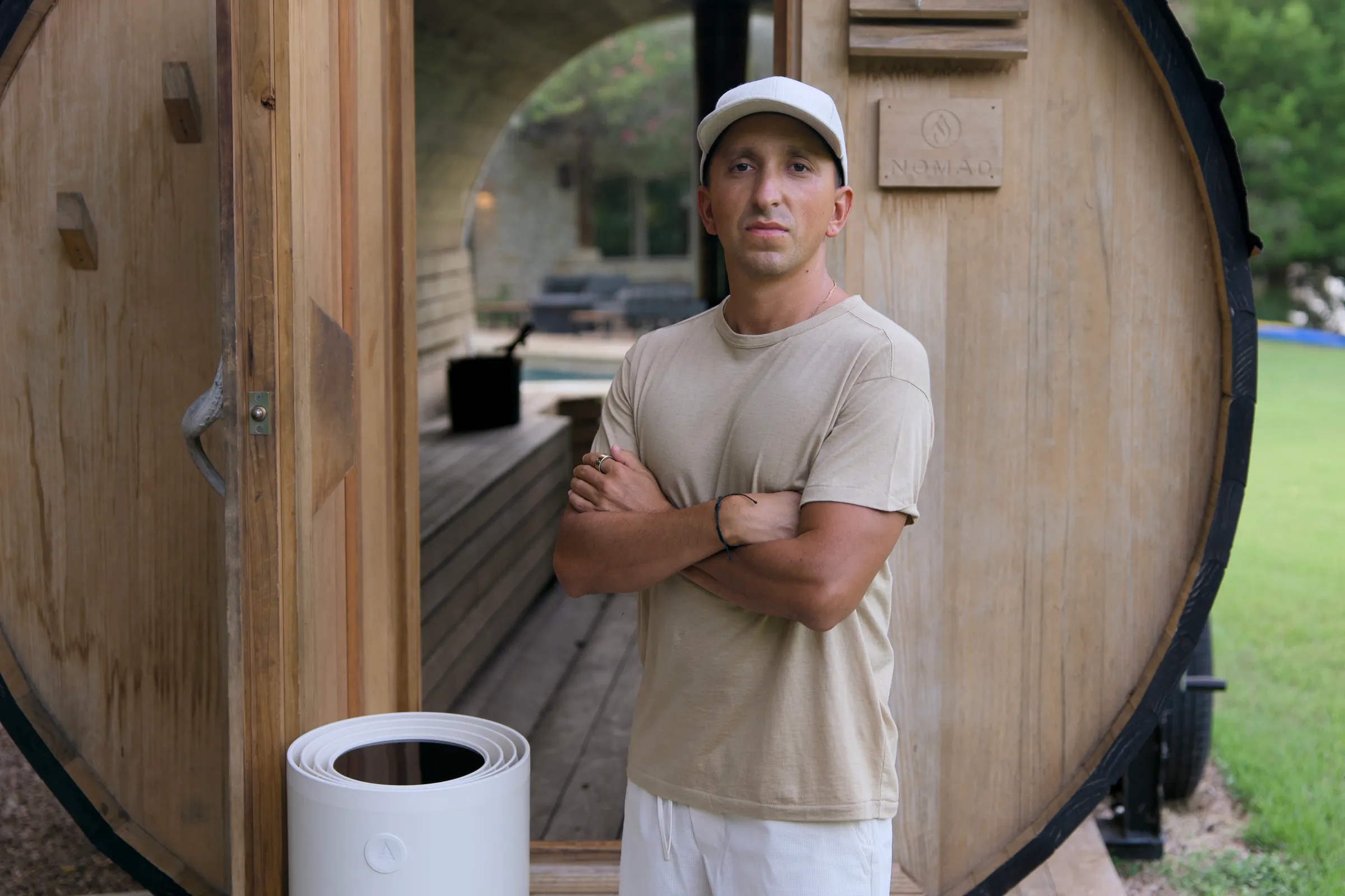 Kyle Lasota standing at the door of his home barrel sauna, arms crossed
